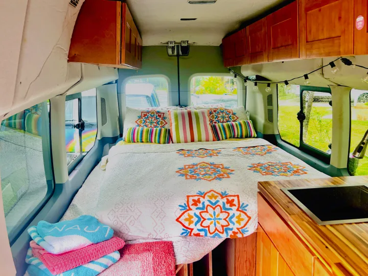 Cozy RV rental interior: colorful bed, compact kitchen, & bright windows. Perfect for travel adventures!. Ford Transit Custom 2016