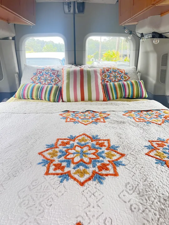 This RV rental offers a stylish, comfy bed featuring a white quilt with colorful mandalas and striped pillows.. Ford Transit Custom 2016