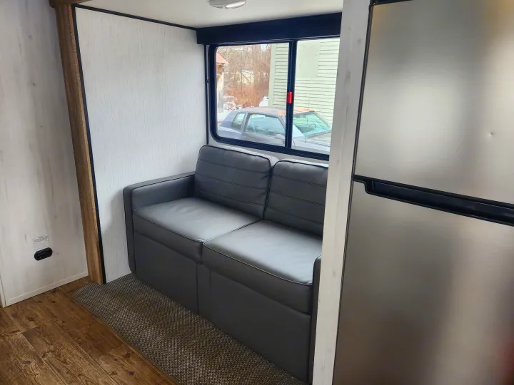 Spacious RV rental interior featuring a comfy gray sofa, large window, and stainless steel refrigerator. Perfect for travel!. Heartland RVs Trail Runner 2022