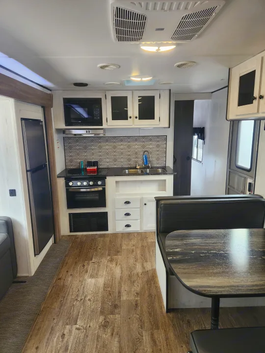 Modern RV rental interior showcasing a well-equipped kitchen with dining area, wood floors, and AC.. Heartland RVs Trail Runner 2022
