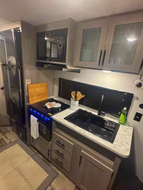 Well-equipped rv rental kitchen featuring a fridge, microwave, stove, sink, and cabinets with patterned glass doors.. Coleman Lantern 2024