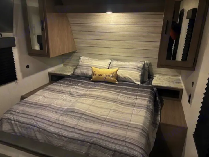 Comfortable RV rental bedroom with striped bedding, 'be our guest' pillow, storage, and nightstands.. Coleman Lantern 2024