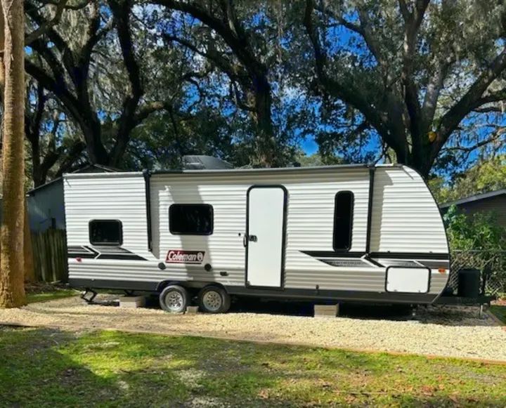 This Coleman travel trailer RV rental is set up at a scenic campsite among trees, ready for your outdoor adventure.. Coleman Lantern 2024