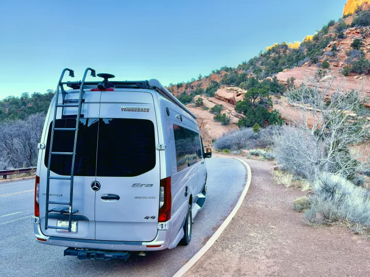 Silver Winnebago Sprinter RV rental parked on a scenic desert road, surrounded by red rock mountains and sparse bushes.. Winnebago Era 2020