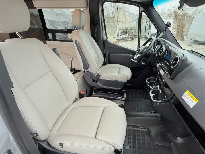 Spacious light-colored leather seats inside a modern RV rental van's front cabin, equipped with advanced airbags.. Winnebago Era 2020