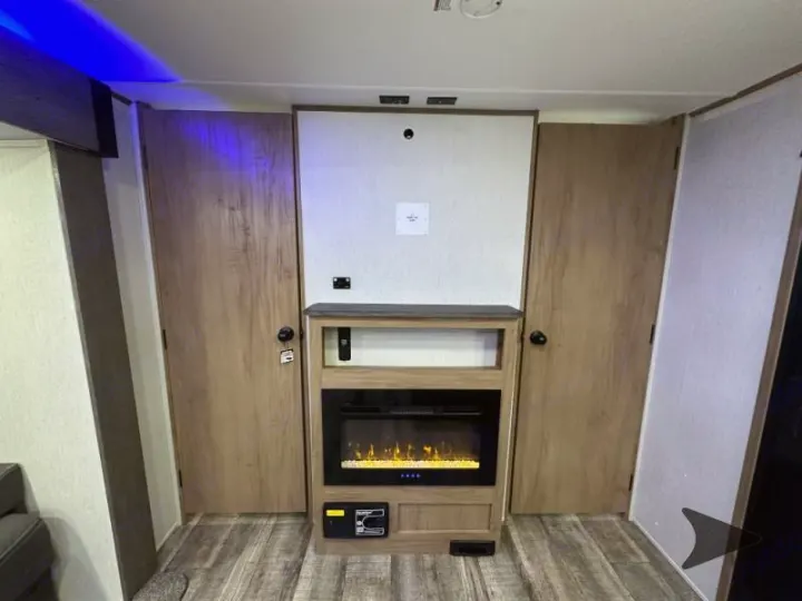 RV rental interior: modern living space featuring an electric fireplace, TV mount, and two private room access doors.. Forest River Cherokee Alpha Wolf 2024