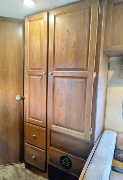 RV rental: Built-in wooden cabinetry, a door, and part of a sofa, providing storage in a compact RV living space.. Coachmen Leprechaun 2015