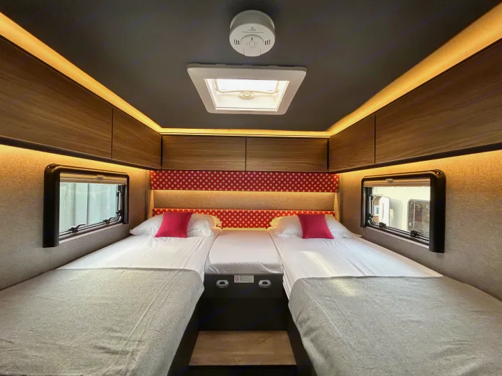 This bright RV rental sleeping area features two single beds, overhead cabinets, windows, a skylight, and ambient lighting.. GlamperRV DBL 2026
