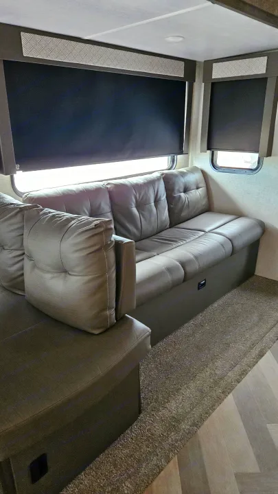 This RV rental features a comfortable grey sofa, dark blinds, textured valances, and soft flooring.. Forest River Wildwood 2021
