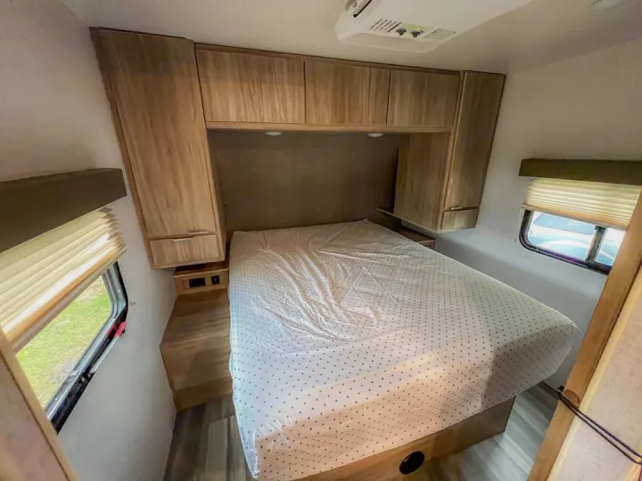 RV rental interior showing a cozy bedroom with a white polka-dot bed, light wood cabinets, and windows with blinds.. Winnebago Minnie Winnie 2021