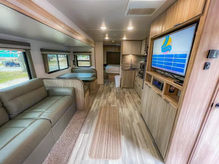 Spacious, modern RV rental interior featuring a comfortable sofa, dinette, kitchen, and TV setup for your travels.. Winnebago Minnie Winnie 2021