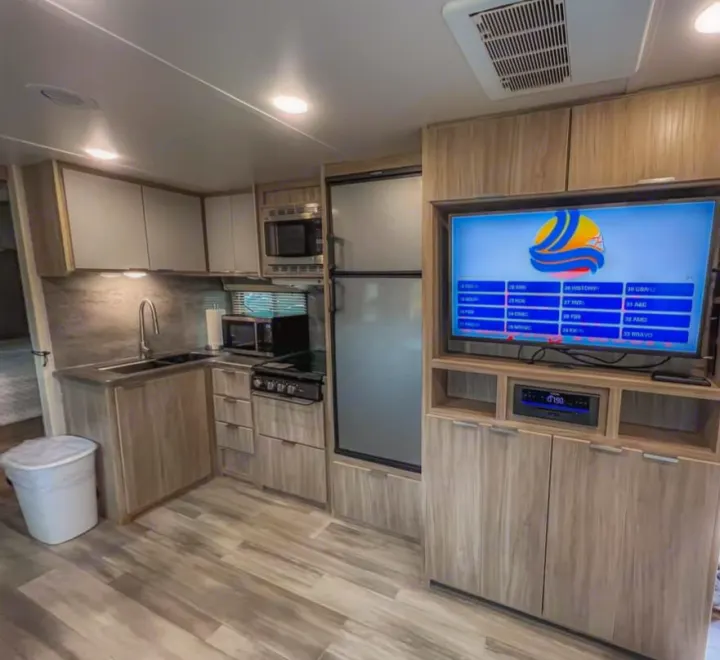This modern rv rental interior features a full kitchen with light wood cabinetry, fridge, and an entertainment center with TV.. Winnebago Minnie Winnie 2021