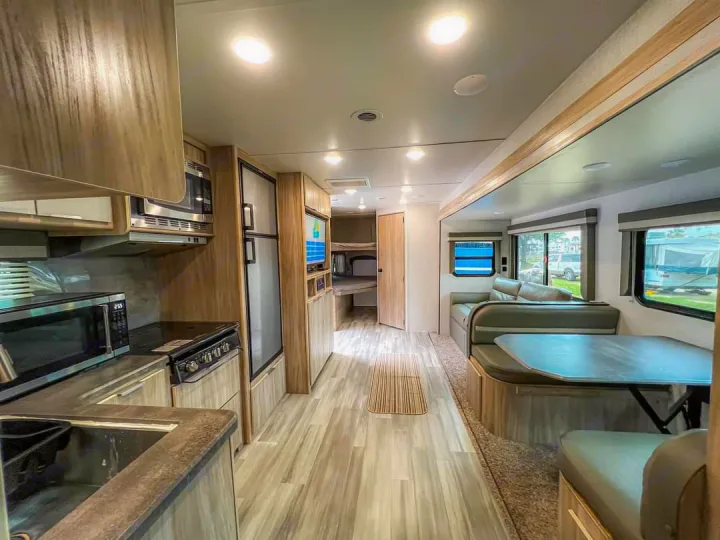 This bright RV rental interior features a modern kitchen, refrigerator, and a comfortable dining/living area. Perfect for travel.. Winnebago Minnie Winnie 2021