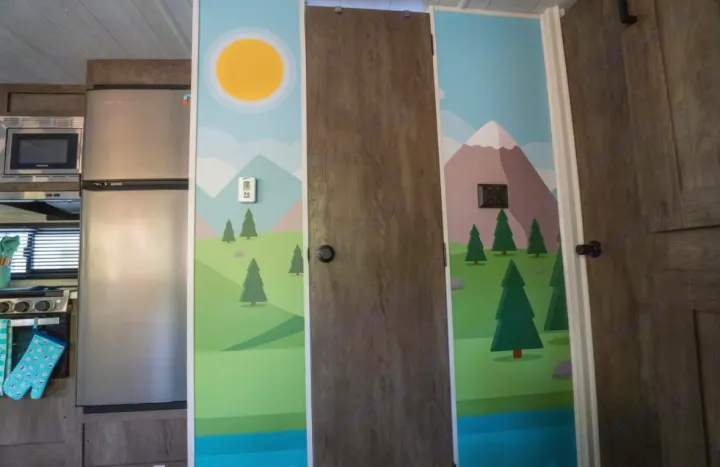 RV rental interior showcases a vibrant mountain mural on walls, complementing the kitchen area with fridge and microwave.. Forest River Salem 2022