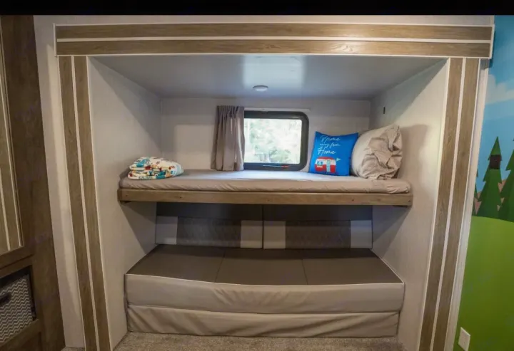 Cozy RV rental bunk beds with a window and a fun pillow, perfect for family travel. Compact sleeping area.. Forest River Salem 2022