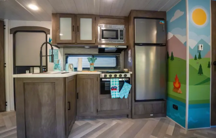 Explore this RV rental's cozy kitchen: wood cabinets, stainless appliances, herringbone floor, and a fun mural.. Forest River Salem 2022