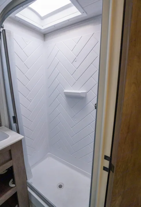 Bright, compact RV rental shower with white herringbone walls, skylight, and soap dish, part of a functional bathroom.. Forest River Salem 2022