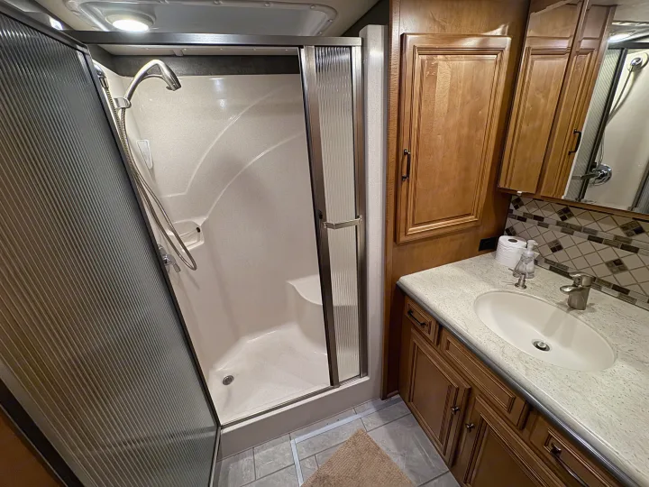 Spacious RV rental bathroom featuring a shower with ribbed doors, and a vanity with a sink, mirror, and storage.. Winnebago Ellipse 2016