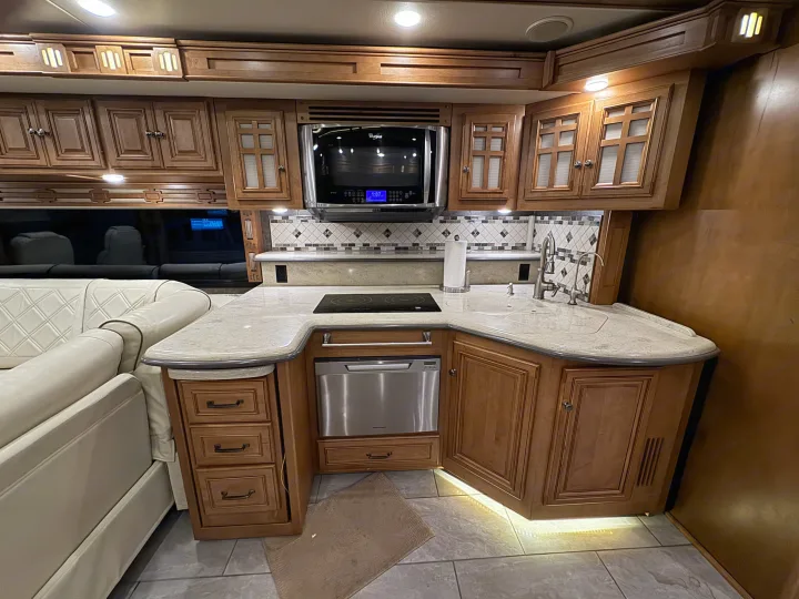 Modern RV rental kitchen interior featuring wood cabinetry, stainless appliances, and a sleek countertop.. Winnebago Ellipse 2016
