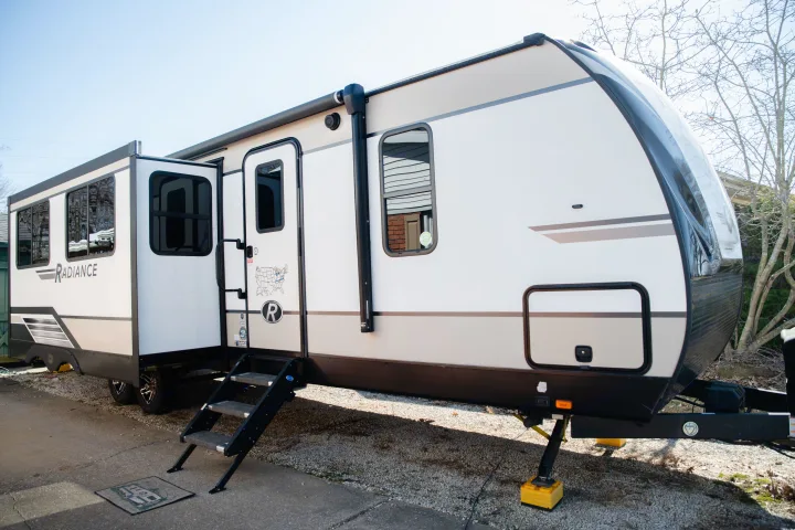 A sleek, modern white and tan RV rental is parked outdoors with its slide-out extended, door open with steps, ready for adventure.. Cruiser RV Radiance Ultra Lite 2020