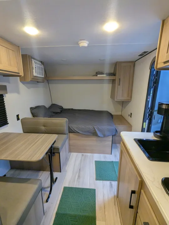 Interior of an RV rental: a cozy space with a bed, dinette, small kitchen, and overhead storage.. Keystone Coleman 2025