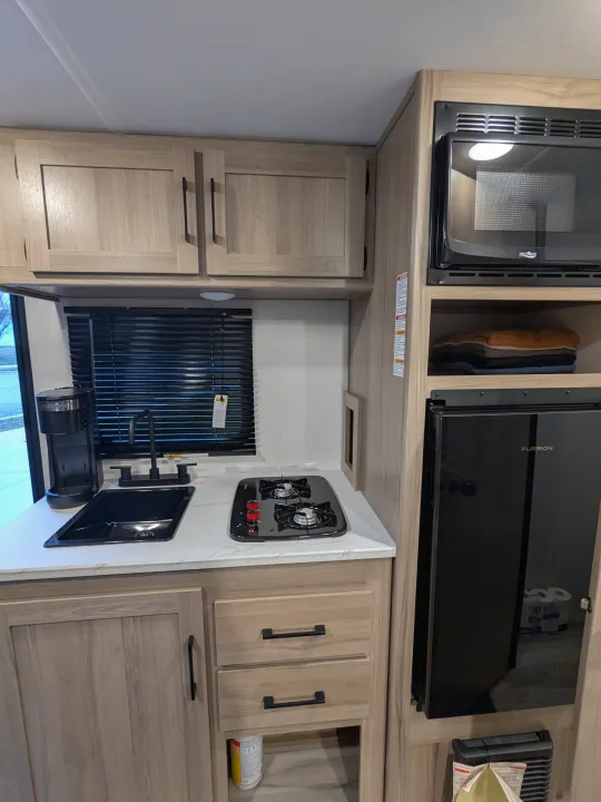 RV rental interior showing a compact kitchenette with sink, stove, microwave, Furrion fridge, and ample cabinets.. Keystone Coleman 2025