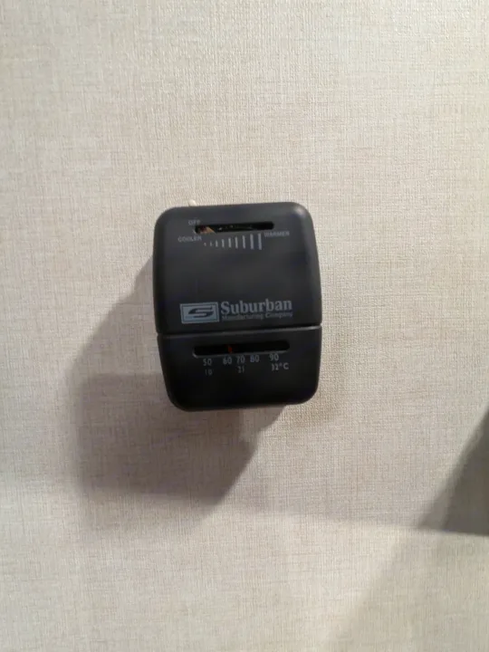 Suburban thermostat in an RV rental, showing temperature settings for cooling and heating with ranges from 50-90°F (10-32°C).. Keystone Coleman 2025
