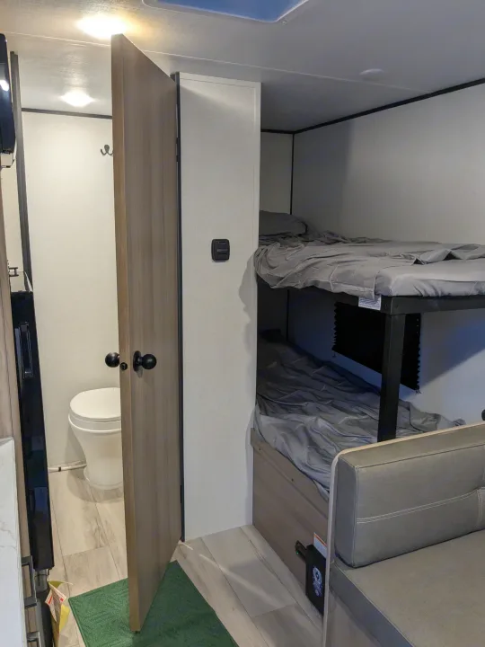 RV rental interior: compact layout with private bathroom, bunk beds, and lounge area. Perfect for family travel.. Keystone Coleman 2025