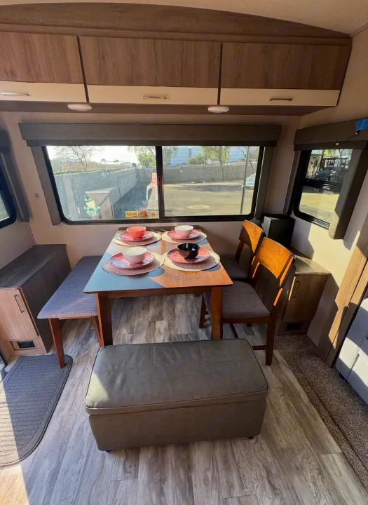 Spacious RV rental dining area with a modern wood table, bench seating, and two chairs, set with pink and black dishes.. Grand Design Imagine 2022