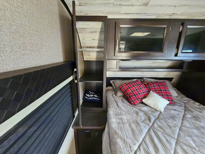 Cozy RV rental bedroom: bed with plaid pillows, overhead cabinets, and side closet storage. Perfect for your travels.. Jayco Jay Feather 2021