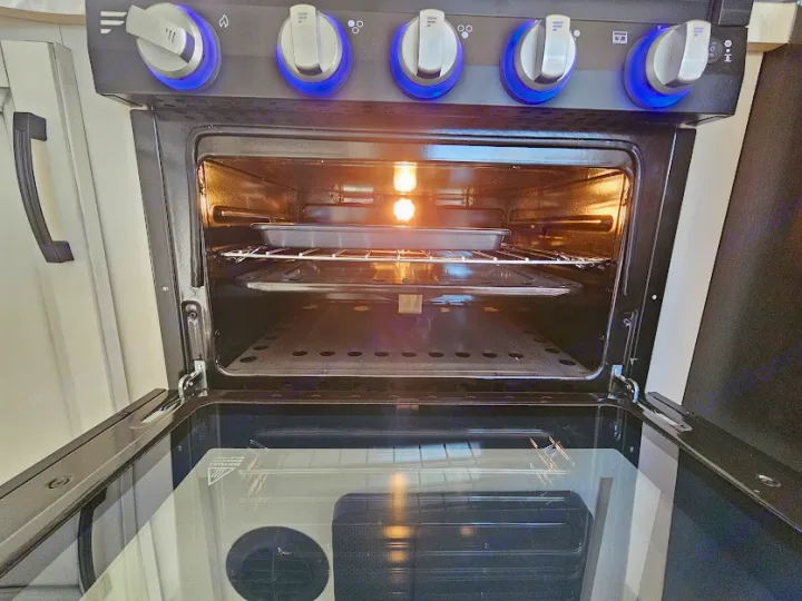 Inside an **RV rental** kitchen oven, an interior light illuminates a baking pan on a rack. Blue LED knobs are visible above.. Jayco Jay Feather 2021
