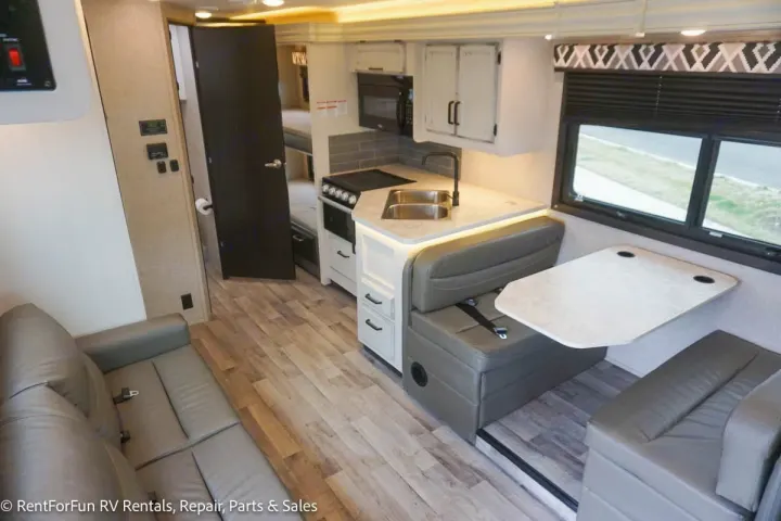 Bright RV rental interior features a modern kitchen, dinette booth with table, comfy sofa, and door to bunks.. Jayco Redhawk 2022