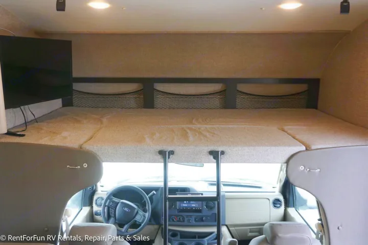 RV rental interior shows over-cab bunk bed, TV, storage nets, and driver's cabin with ladder.. Jayco Redhawk 2022