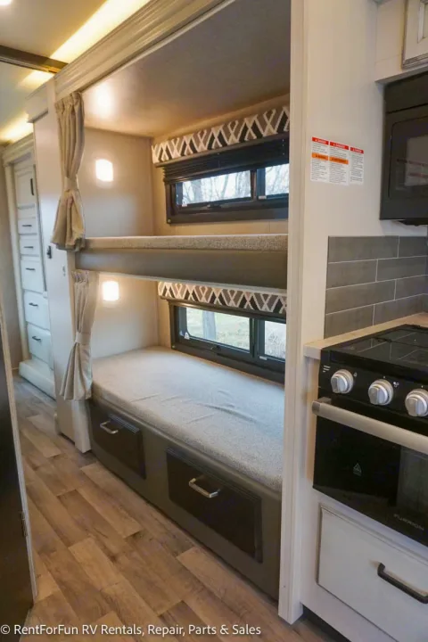 Inside this RV rental, find cozy bunk beds with windows, built-in storage, and a compact kitchen area.. Jayco Redhawk 2022