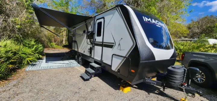 Modern Imagine rv rental travel trailer set up at a shaded campsite, awning extended with an outdoor rug, ready for adventure.. Grand Design Imagine 2800BH 2025
