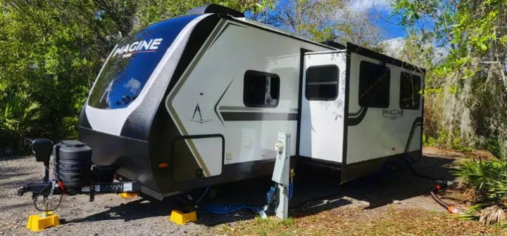 This Imagine travel trailer, a perfect RV rental option, is fully set up at a scenic campsite with utilities.. Grand Design Imagine 2800BH 2025