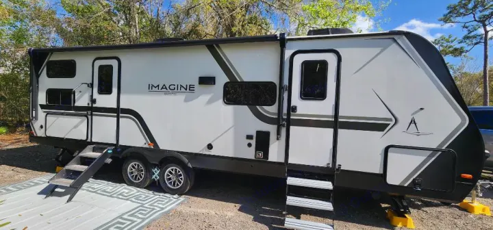 Large white and black Imagine travel trailer RV rental parked outdoors on gravel, featuring two entry doors and steps.. Grand Design Imagine 2800BH 2025