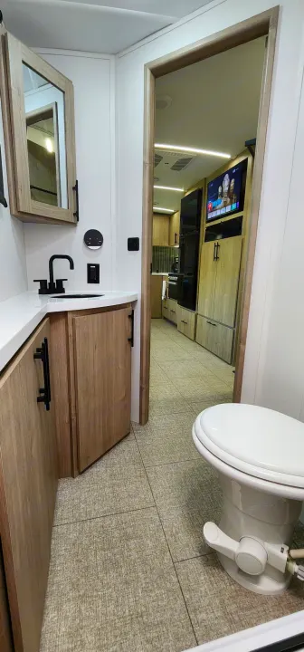 Modern RV rental: bathroom with vanity & toilet, looking into a sleek kitchen & living area with TV.. Grand Design Imagine 2800BH 2025