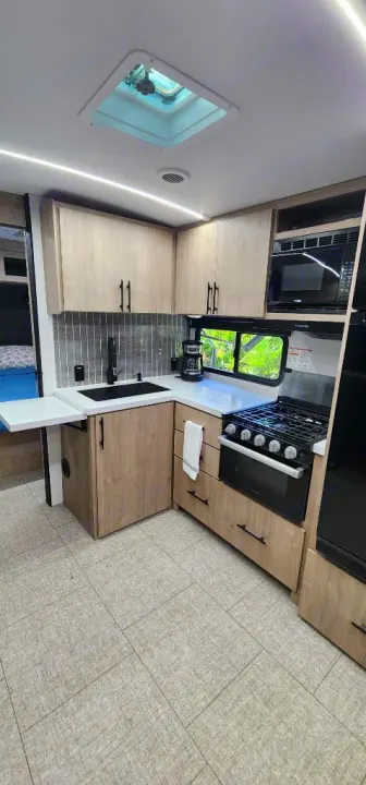 Modern RV rental kitchen with light wood cabinets, black appliances, tile backsplash, and plank flooring.. Grand Design Imagine 2800BH 2025