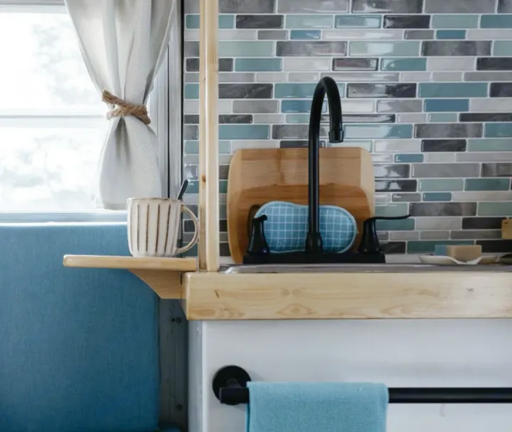 Compact RV rental kitchen with blue tile backsplash, sink, window view, and cozy bench seating. Ready for adventure!. Boler Boler 1974