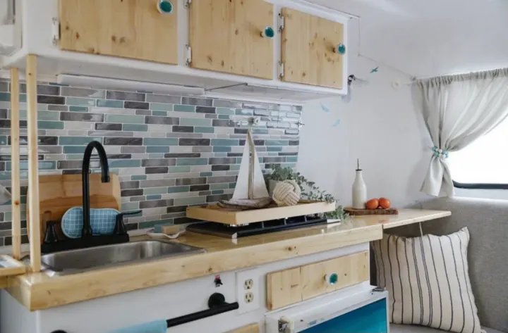 Modern RV rental kitchen with wooden counters, blue-gray tile backsplash, sink, and cozy seating.. Boler Boler 1974