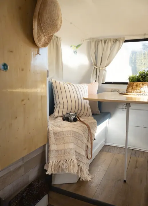 Bright RV rental interior featuring a wooden door, bench with cozy pillows & knit blanket, and a table with a plant.. Boler Boler 1974