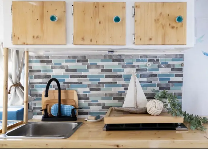 RV rental kitchen: light wood cabinets, sink, blue tile backsplash, and nautical decor. Compact and cozy.. Boler Boler 1974