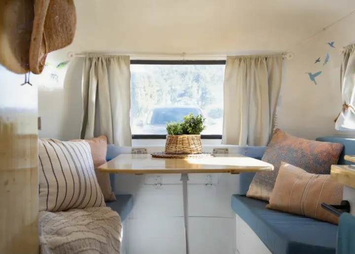 Inside a cozy RV rental: dining booth with blue seats, wood table, and plant, ready for adventure.. Boler Boler 1974