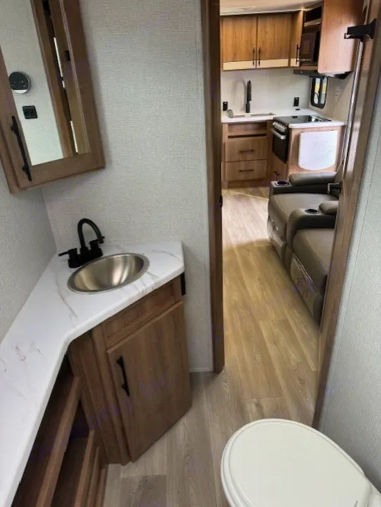 RV rental interior featuring a compact bathroom with a sink, mirror, and toilet, leading to a kitchen and recliners.. Grand Design Imagine 2024