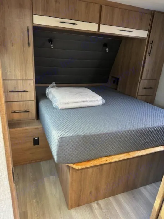 RV rental: inviting bedroom featuring a quilted grey mattress, padded headboard, and wood-toned built-in storage.. Grand Design Imagine 2024