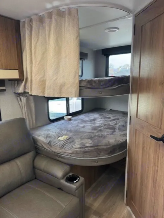 Cozy RV rental interior with bunk beds, a privacy curtain, and a comfortable recliner seat, ideal for family travel.. Grand Design Imagine 2024