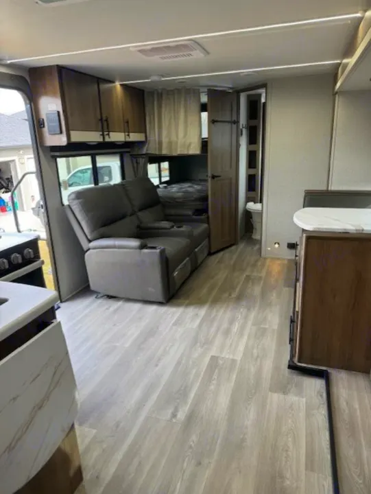 Clean and modern rv rental interior with a living area, recliner sofa, kitchen, and light wood flooring. Bedroom/bath visible.. Grand Design Imagine 2024
