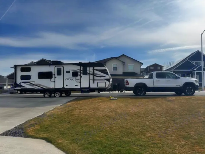 White pickup truck towing a Grand Design Imagine travel trailer. This RV rental is ready for your next adventure.. Grand Design Imagine 2024