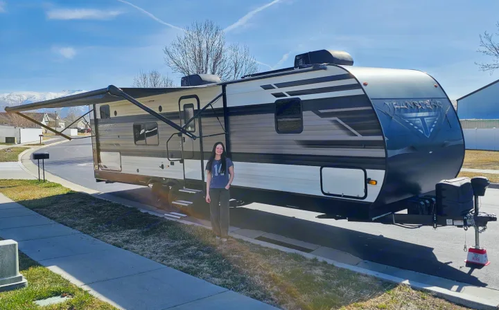 Young woman poses with her RV rental, ready for travel adventures. Snow-capped mountains frame the background.. Grand Design Transcend Xplor 2022